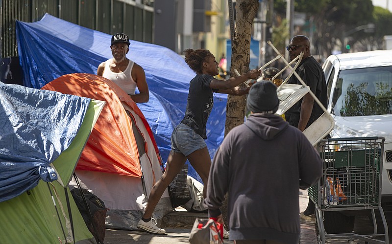 A homeless woman throws a plastic chair in the air downtown Los Angeles Tuesday, Sept. 17, 2019. Los Angeles Mayor Eric Garcetti says he hopes President Donald Trump will work with the city to end homelessness as the president visits California for a series of fundraisers. Garcetti says the federal government could aid Los Angeles with surplus property or money to create additional shelters. Garcetti says he has not been invited to meet with the president. in Los Angeles (AP Photo/Damian Dovarganes)