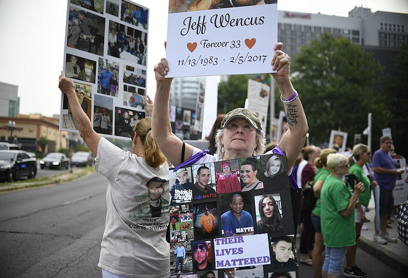 FILE - In this Aug. 17, 2018, file photo, Lynn Wencus of Wrentham, Mass., holds a sign with a picture of her son Jeff and wears a sign of others' loved ones lost to OxyContin and other opioids during a protest at Purdue Pharma LLP headquarters in Stamford, Conn. Some of the money in Purdue Pharma’s proposed multibillion-dollar opioid settlement would come from the continued sale of opioids. “It’s blood money paying for blood money,” said Wencus. “It’s ludicrous. The whole thing would be almost comical if we weren’t talking about human lives here.” (AP Photo/Jessica Hill, File)
