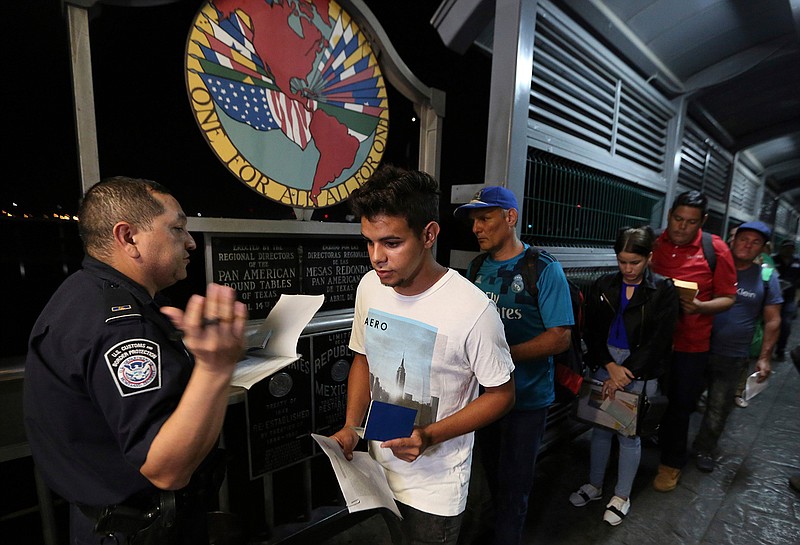 Cuban Abel Oset Jr., center, and his father Abel Oset, behind him, show their identification to a U.S. Customs and Border Protection officer before their appointments to apply for asylum in United States, as they cross International Bridge 1 to leave Nuevo Laredo, Mexico and enter Laredo, Texas, Tuesday, Sept. 17, 2019. Tent courtrooms opened Monday in two Texas border cities to help process thousands of migrants who are being forced by the Trump administration to wait in Mexico while their requests for asylum wind through clogged immigration courts. (AP Photo/Fernando Llano)