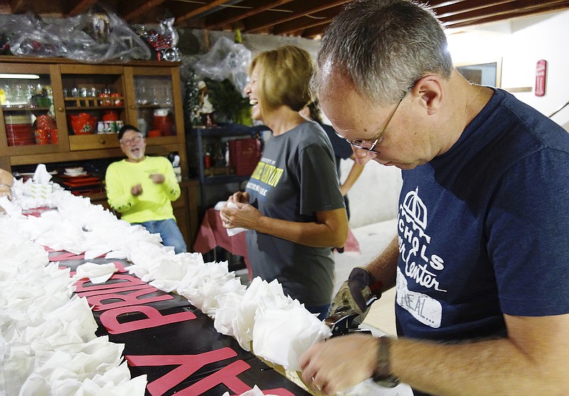 Nicole Roberts/News Tribune
Bill Hawley, background, and Cheryl Wolf share a laugh while Bryan Wolf staples tissue paper flowers on a board. They are just three of several dozen retired Jefferson City School District faculty and staff have spent numerous hours building a frame and creating paper flowers to install on it to make a float for Thursday's annual JC Homecoming Parade. 