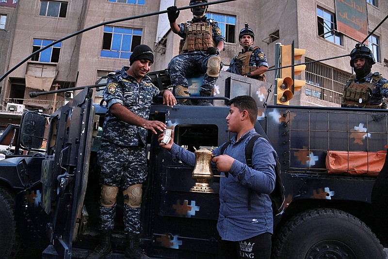 A street vendor sells coffee to the Iraqi Federal police as they deployed in Sadr City, Baghdad, Iraq, Monday, Oct. 7, 2019. Iraq's prime minister on Monday ordered the police to replace the army in Sadr City, a heavily populated Shiite neighborhood of Baghdad where dozens of people were killed or wounded in weekend clashes stemming from anti-government protests. (AP Photo/Hadi Mizban)