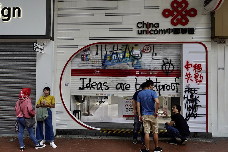 Staff from China Unicom mobile network clean outside the shop as it was damaged during a weekend protest in Hong Kong, Monday, Oct. 7, 2019. Tens of thousands of masked protesters marched defiantly in the city center Sunday, but the peaceful rallies quickly degenerated into chaos at several locations as hard-liners again lobbed gasoline bombs, started fires and trashed subway stations and China-linked banks and shops. (AP Photo/Vincent Yu)