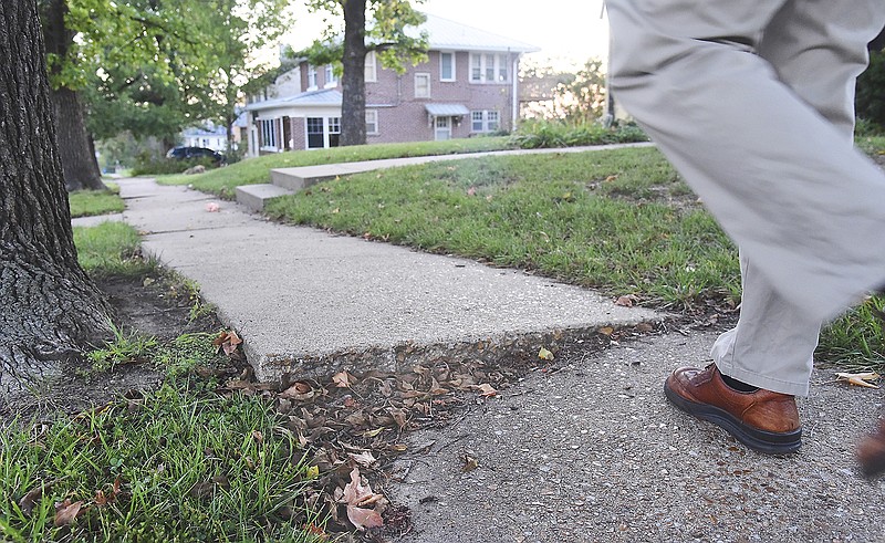 A pedestrian walks on the sidewalks adjacent to Adams Street. Tree roots have pushed up the concrete in areas, making for an uneven and possibly dangerous path. The Jefferson City Council voted on a substitute bill regarding the vertical displacement of sidewalks. 