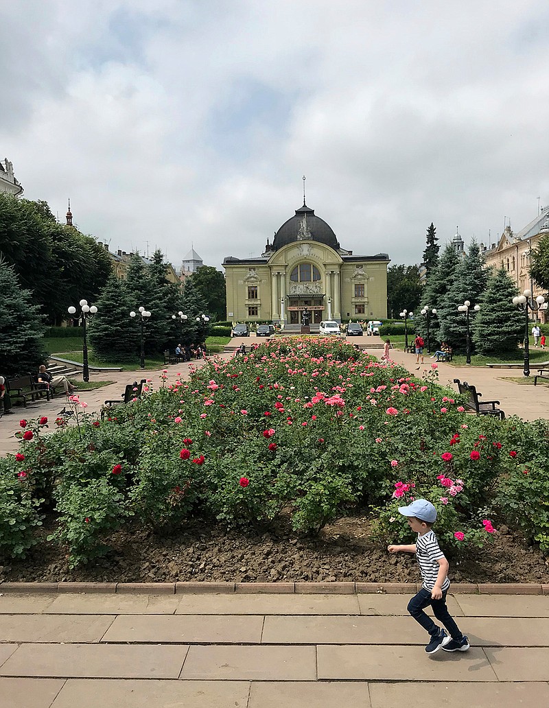 This June 23, 2019 photo shows a child running in front of a bed of roses as the Chernivtsi Drama Theater stands in the background, in Chernivtsi, Ukraine. Tucked in the southwest corner of Ukraine, Chernivtsi is a cheerful city that graciously marries the glories and sorrows of centuries past with vibrant Eastern European urban life today. (AP Photo/Frances D'Emilio)