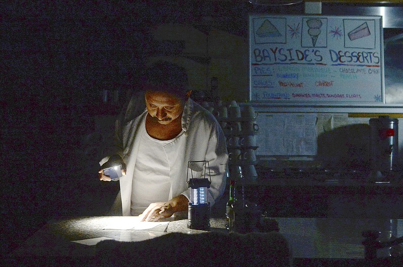 Carlos Lama of Bayside Cafe, which was among businesses to lose power due to PG&E's public safety power shutoff, uses an LED lamp and light from his phone at the counter of the restaurant in Sausalito, Calif., Wednesday, Oct. 9, 2019. Pacific Gas & Electric has cut power to more than half a million customers in Northern California hoping to prevent wildfires during dry, windy weather throughout the region. (Alan Dep/Marin Independent Journal via AP)