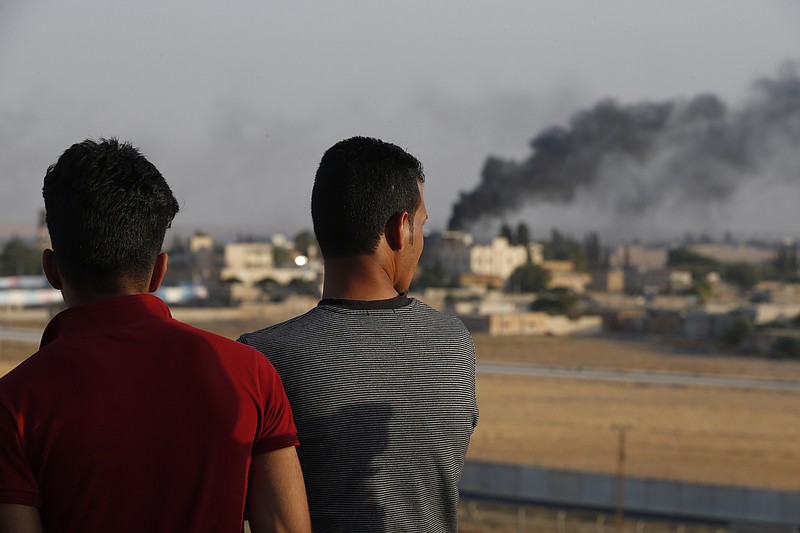 People standing on a rooftop in Akcakale, Sanliurfa province, southeastern Turkey, at the border with Syria, watch as in the background smoke billows from fires caused by Turkish bombardment in Tal Abyad, Syria, Sunday, Oct. 13, 2019.  Turkey's official Anadolu news agency says Turkey-backed Syrian forces have advanced into the center of a Syrian border town, Tal Abyad, on the fifth day of the Turkey's military offensive against Kurdish fighters in Syria. (AP Photo/Lefteris Pitarakis)