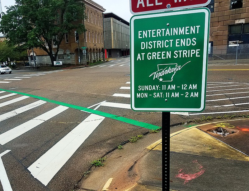 A sign and a green stripe painted on the pavement mark the border of Texarkana, Arkansas' new entertainment district Tuesday, Oct. 15, 2019, at the corner of East Third Street and North State Line Avenue. A new law passed during the recent state legislative session allowed the city to establish the district, where outdoor alcohol consumption from open containers is allowed.