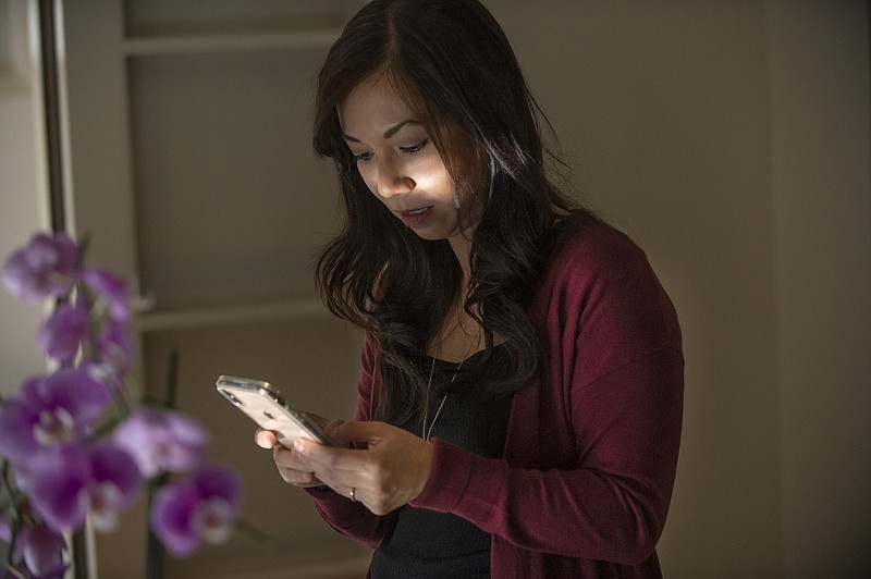 In this Wednesday Aug. 28, 2019 photo, emergency room physician, Dr. Anna Nguyen uses her smartphone to communicate with a remote patient from her Sacramento, Calif., home. The medical industry is seeing a growing form of care where doctors diagnose, treat and prescribe through secure text messages. (AP Photo/Randall Benton)