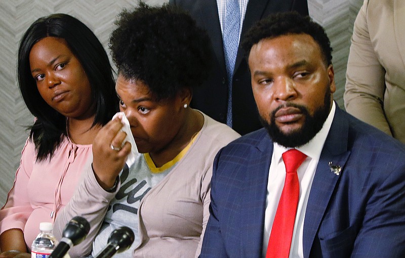 Amber Carr, center, wipes a tear as her sister, Ashley Carr, left, and attorney Lee Merritt, right, listen to their brother Adarius Carr talk about their sister, Atatiana Jefferson during a news conference Monday, Oct. 14, 2019 in downtown Dallas. The family of the 28-year-old black woman who was shot and killed by a white police officer in her Fort Worth home as she played video games with her 8-year-old nephew expressed outrage that the officer has not been arrested or fired. (Irwin Thompson/The Dallas Morning News via AP)