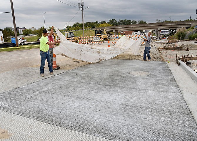 With afternoon rain clouds looming overhead, a crew from Donnie Schnieders Construction puts plastic over the freshly poured concrete Tuesday on Dunklin Street. The Dunklin Street project has faced numerous issues over the duration of the work likely causing the bridge demolition and construction to be on hold until spring.
