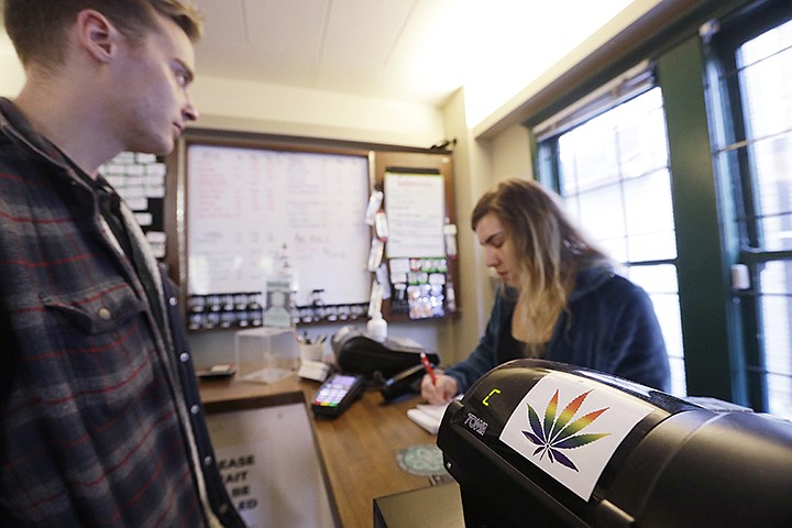 In this photo taken Wednesday, Oct. 9, 2019, clerk Jayme Wilton, right, assists a customer at the Medicinal Cannabis Dispensary, an unlicensed marijuana shop, in Vancouver, B.C.. (AP Photo/Elaine Thompson)