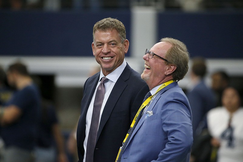 In this Sept. 8, 2019, file photo, broadcast personality Troy Aikman, left, talks with sports reporter Ed Werder, right, before an NFL football game between the New York Giants and Dallas Cowboys in Arlington, Texas. There are few things Aikman hasn't done in the sport of football. The Dallas Morning News reports the 52-year-old has three Super Bowl rings, six Pro Bowl appearances, a Walter Payton NFL Man of the Year Award and spots in the Pro Football and College Football Halls of Fame. He was also the No. 1 pick in the 1989 NFL draft and is Fox's top NFL color commentator. The only thing missing from his résumé? Coaching. This year, though, the Cowboys legend decided to give it a shot as the quarterbacks coach at the Episcopal School of Dallas, where a stepson plays. (AP Photo/Michael Ainsworth, File)