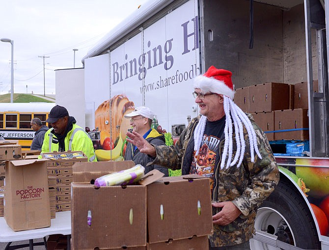Randy Edwards wears a holiday cap to entertain the public as he and other volunteers from Scholastic Inc. hand out produce during a mobile food pantry  last week at the Jefferson City Boys & Girls Club.