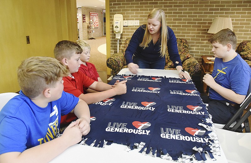 Fifth-grade teacher Annie Ziegelbein demonstrates for students how they'll tie the cut ends of the quilt they are preparing to give away. Clockwise from left, students Henry Salmons, Connor McPeak, Wesley Marsh and Parker Roettgen attend Trinity Lutheran School and performed service work Wednesday — in school and at other locations. Fifth-graders tied cut ends of small quilts that will be taken to wheelchair-bound residents at Heisinger Bluffs and St. Joseph Bluffs. The quilts were made of T-shirts cut into sections and sewn together. The shirts are left over from different Thrivent-sponsored events and activities. After they're sewn together, a piece of fleece is sewn to the back after which a series of cuts are made around the edges. A student's grandmother volunteered her time to cut the shirts and sew the quilts. 
