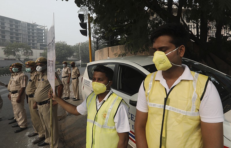 Volunteers and policemen wear pollution masks and stand at a busy crossing with the banner saying obey odd and even, remove pollution, in New Delhi, India, Monday, Nov. 4, 2019. Authorities in New Delhi are restricting the use of private vehicles on the roads under an "odd-even" scheme based on license plates to control vehicular pollution as the national capital continues to gasp under toxic smog. (AP Photo/Manish Swarup)