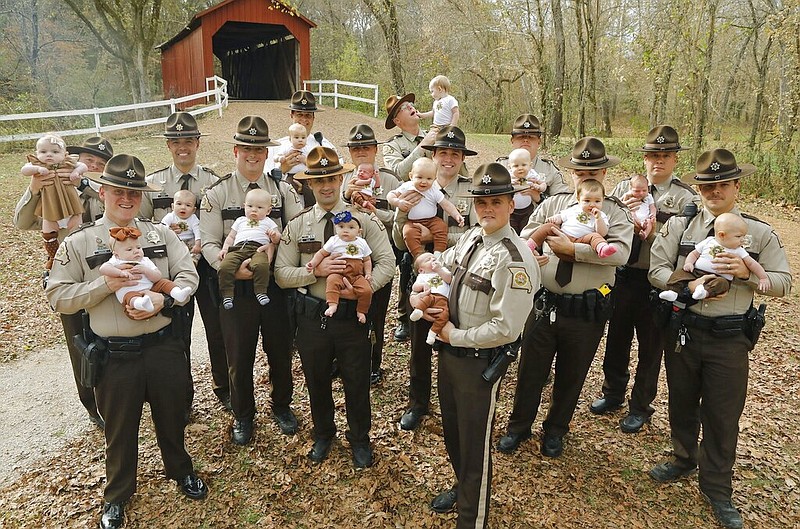 In this Nov. 4, 2019, photo fourteen Jefferson County Sheriffs Deputies pose for a photo with their babies at the Sandy Creek Covered Bridge in Jefferson County, Mo. They are from left, with their babies: Adam Lambrich with Lilliana; AJ Kausler with Lucy; Matt Moore with Luca; Scott Ehrhard with Hudson; Andy Sides with Carter; Greg Bohn with Evelyn; Dustin Isenhart with Kash; Nick Gamm with Gweneth; Colby McCreary with Sawyer; Cody Cawvey with Micah; Shawn Loness with Connor; Andrew Griffon with Kinsley; Kevin Karl with Kade; and Roger Waeckerle with Wyatt. (J.B. Forbes/St. Louis Post-Dispatch via AP)