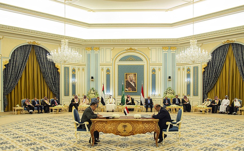 In this photo released by the Saudi Royal Palace, Yemeni Southern Transitional Council member and former Aden Governor Nasser al-Khabji, left, and Yemen's deputy Prime Minister Salem al-Khanbashi sign a power-sharing deal  in Riyadh, Saudi Arabia, Tuesday, Nov. 5, 2019. Yemen's internationally recognized government signed a power-sharing deal with Yemeni separatists that are backed by the United Arab Emirates. A picture of Saudi Arabia's founder late King Abdul Aziz Al Saud hangs on wall. (Bandar Aljaloud/Saudi Royal Palace via AP)