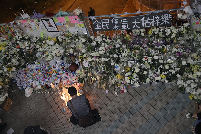 A protester light candles near flowers and a banner which reads "From all of us - God bless Chow Tsz-Lok" at the site where student Chow Tsz-Lok fell during a recent protest in Hong Kong on Friday, Nov. 8, 2019. Chow, a Hong Kong university student who fell off a parking garage after police fired tear gas during clashes with anti-government protesters died Friday in a rare fatality after five months of unrest, fueling more outrage against authorities in the semi-autonomous Chinese territory. (AP Photo/Kin Cheung) ///