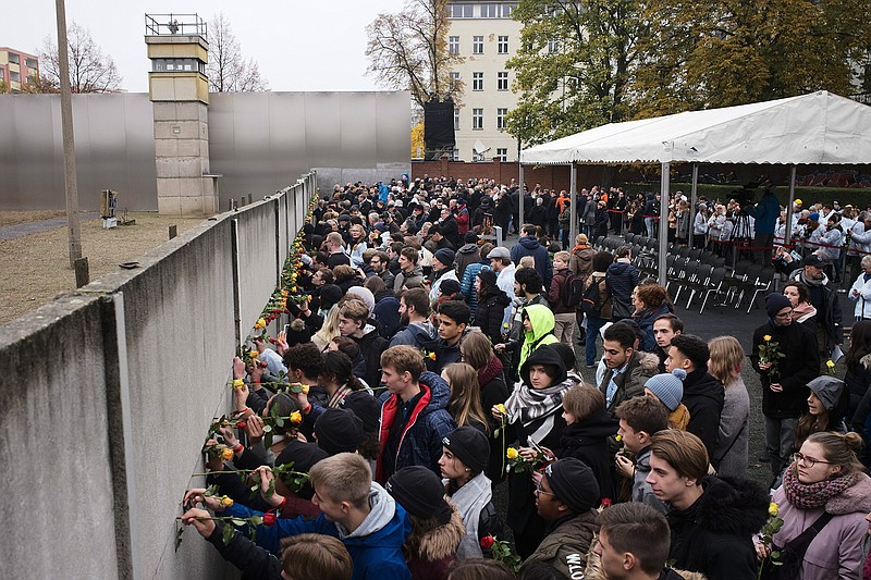 Young people stuck flowers in remains of the Berlin Wall during a commemoration ceremony to celebrate the 30th anniversary of the fall of the Berlin Wall at the Wall memorial site at Bernauer Strasse in Berlin, Saturday, Nov. 9, 2019. (AP Photo/Markus Schreiber)
