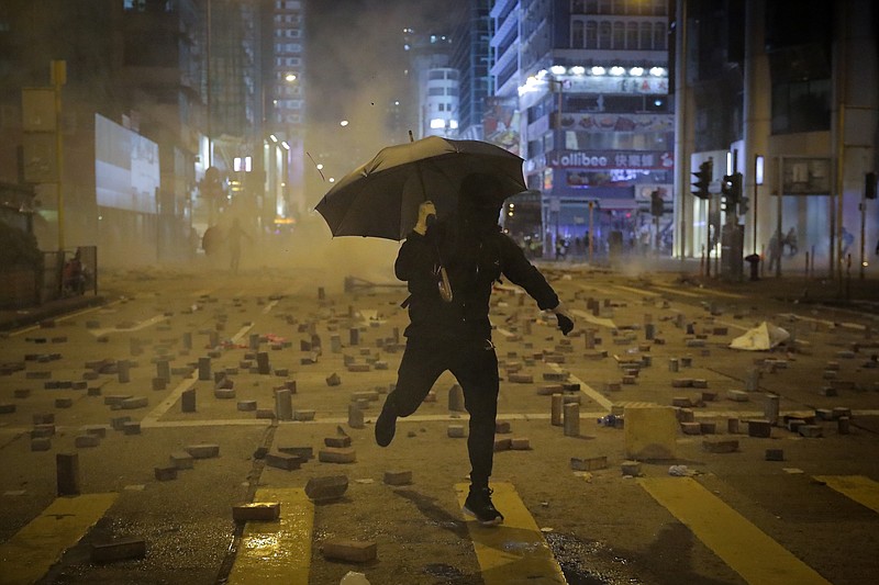 A protester with an umbrella runs away from tear gas fired by riot police on a street scattered with bricks during a protests in Hong Kong, Monday, Nov. 11, 2019. Hong Kong's leader Carrie Lam has pledged to "spare no effort" in bringing an end to anti-government protests that have wracked the city for more than five months, following a day of violence in which one person was shot and another set on fire. (AP Photo/Kin Cheung)