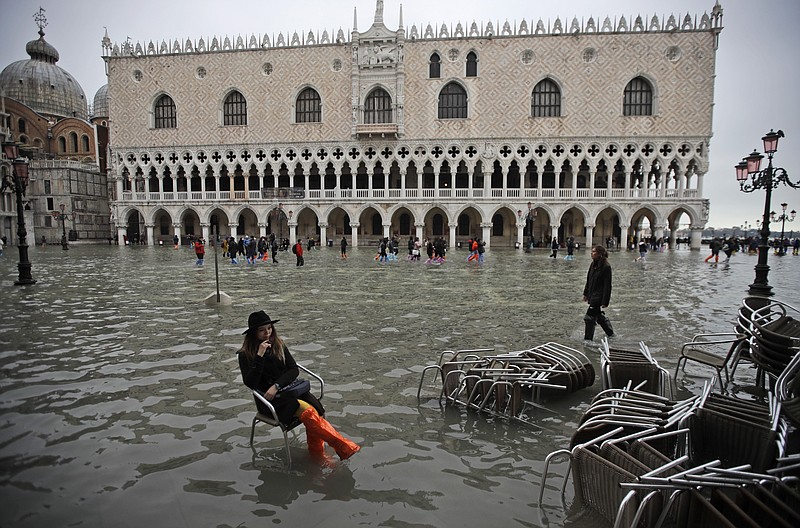 A woman sits in a chair in a flooded St. Mark's Square, in Venice, Wednesday, Nov. 13, 2019. The high-water mark hit 187 centimeters (74 inches) late Tuesday, Nov. 12, 2019, meaning more than 85% of the city was flooded. The highest level ever recorded was 194 centimeters (76 inches) during infamous flooding in 1966. (AP Photo/Luca Bruno)