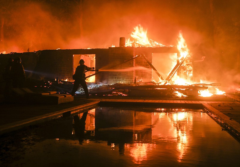 FILE - In this Friday, Nov. 9, 2018 file photo, a firefighter battles the Woolsey Fire burning a home in Malibu, Calif. A Southern California utility has agreed to pay $360 million to settle lawsuits brought by cities, counties and other public agencies over deadly wildfires sparked by its equipment in the last two years, including one that was later blamed for a mudslide that killed more than 20 people. An attorney for 23 public entities said Wednesday, Nov. 13, 2019, that Southern California Edison has agreed to the sum to repay taxpayers for firefighting and damage from the Thomas Fire in 2017 and Woolsey Fire last year. (AP Photo/Ringo H.W. Chiu, File)