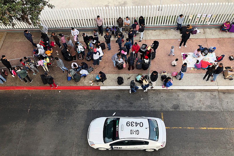 In this Nov. 10, 2019, photo, migrants gather at the U.S.-Mexico border in Tijuana, Mexico, to hear names called from a waiting list to claim asylum in the U.S. The U.S. has sent a Honduran migrant back to Guatemala in a move that marked a new phase of President Donald Trump's immigration crackdown. (AP Photo/Elliot Spagat)