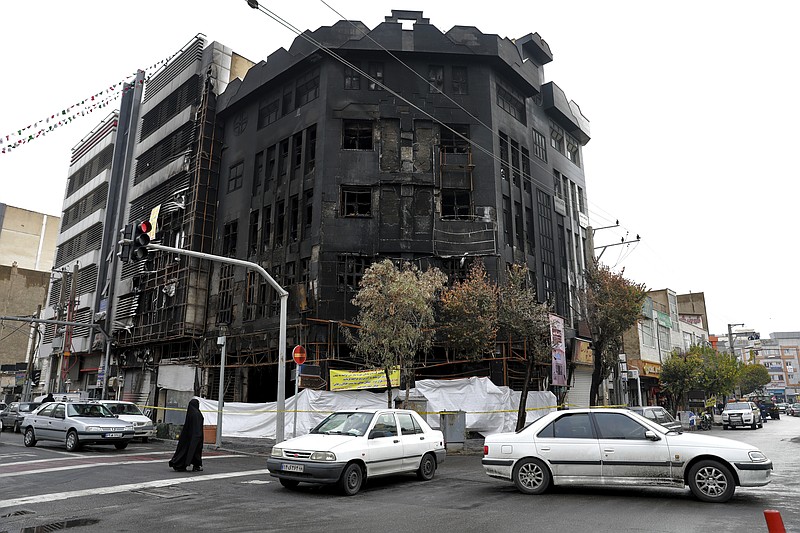 FILE - In this Wednesday, Nov. 20, 2019 file photo, traffic passes a building that was set ablaze during recent protests over government-set gasoline prices rises, in Tehran, Iran. As Iran restores the internet after a weeklong government-imposed shutdown, new videos purport to show the demonstrations over gasoline prices rising and the security-force crackdown that followed. The videos offer only fragments of encounters, but they fill in the larger void left by Iran’s state-controlled television and radio channels. On their airwaves, hard-line officials allege foreign conspiracies and exile groups instigated the unrest that began Nov. 15. (AP Photo/Ebrahim Noroozi, File)