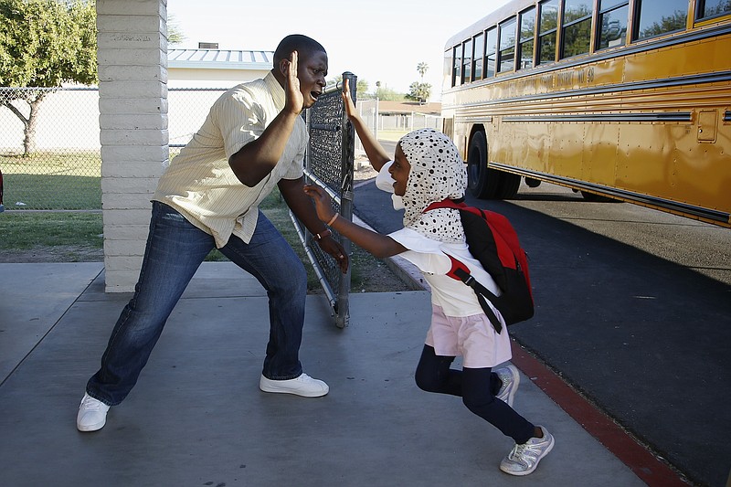 Samuel Lavi, left, a Congolese native who is a teaching assistant and family engagement liaison, greets first grader Kediga Ahmed as she arrives at the Valencia Newcomer School attend class Thursday, Oct. 17, 2019, in Phoenix. Children from around the world are learning the English skills and American classroom customs they need to succeed at so-called newcomer schools. Valencia Newcomer School in Phoenix is among a handful of such public schools in the United States dedicated exclusively to helping some of the thousands of children who arrive in the country annually.   (AP Photo/Ross D. Franklin)