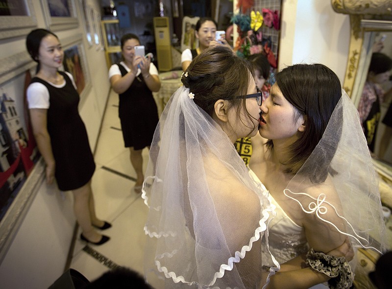FILE - In this July 2, 2015, file photo, Teresa Xu, left, and Li Tingting, right, share a kiss as clerks take photographs in a beauty salon where the two were preparing for their wedding in Beijing. LGBT activists in China are seeking to legalize same-sex marriage through a novel tactic: submitting opinions on a draft new civil code to the country’s legislature. (AP Photo/Mark Schiefelbein, File)