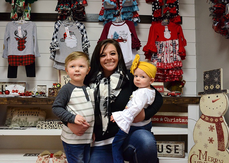 Brittny Gibson kneels next to her children Tucker, 3, and Riley, 1, Tuesday, Nov. 26, 2019, inside her new business, Brittny's Bowtique, in Holt Summit. 