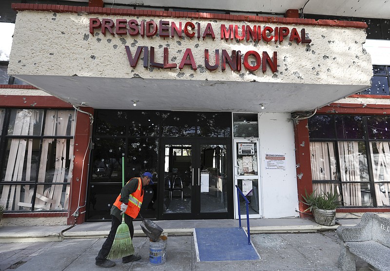 A worker cleans up outside City Hall, riddled with bullet holes, in Villa Union, Mexico, Monday, Dec. 2, 2019. The small town near the U.S.-Mexico border began cleaning up Monday even as fear persisted after 22 people were killed in a weekend gunbattle between a heavily armed drug cartel assault group and security forces. (AP Photo/Eduardo Verdugo)