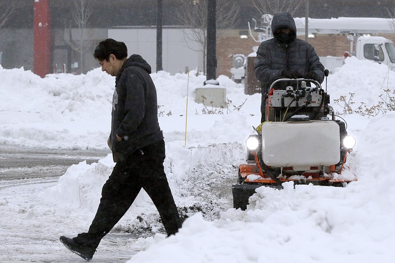 A pedestrian makes their way through a parking lot where snow is being cleared after an overnight snowfall, Monday, Dec. 2, 2019, in Marlborough, Mass. (AP Photo/Bill Sikes)