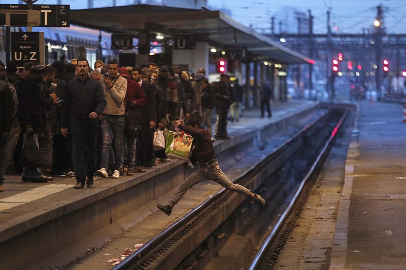 FILE - In this Tuesday, April 3, 2018 file photo a passenger crosses railroad tracks at rush hour at Gare de Lyon train station, in Paris. France's rail operator SNCF and the Paris Metro say nationwide strikes will wipe out most services Thursday, impacting millions. The SNCF expects that 9 out of 10 high-speed trains won't run and that half of the Eurostar services linking France and Britain will be canceled, too. (AP Photo/Francois Mori, File)