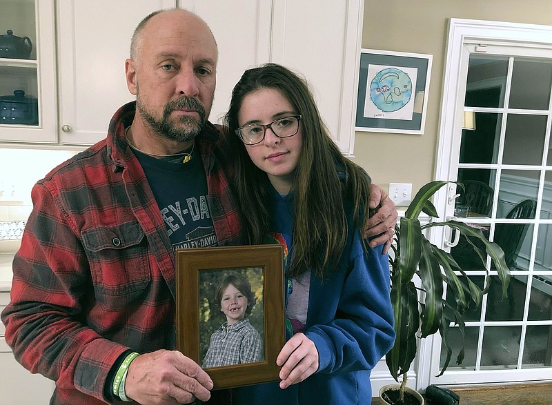 In this Dec. 3, 2019, photo, Mark Barden and his daughter Natalie Barden hold a photograph of Natalie's late brother, Daniel, at their home in Newtown, Conn. Daniel died in the Dec. 14, 2012, Sandy Hook Elementary School shooting that killed 20 first graders and six educators. Natalie, 17, is among Newtown students who have grown up to become young voices in the gun violence prevention movement. (AP Photo/Dave Collins)