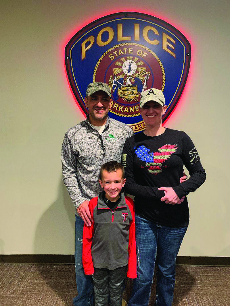 Holly Smith poses for a photo with her husband, Billy, and their son, Ian, at the Texarkana, Ark., Police Department. Holly is now tumor-free after being diagnosed with an aggressive gliobastoma in April. The Smiths are both TAPD officers.