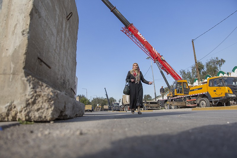 A woman passes by Iraqi security forces while they remove cement blocks and open the streets, that were closed for security concerns, around the Green Zone in Baghdad, Iraq, Thursday, Jan. 2, 2020. Iran-backed militiamen have withdrawn from the U.S. Embassy compound in Baghdad after two days of clashes with U.S. security forces. (AP Photo/Nasser Nasser)