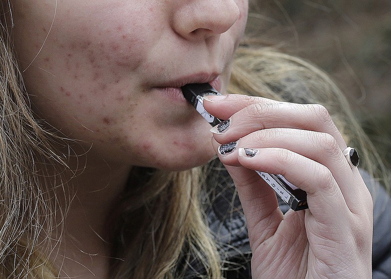 FILE - In this April 11, 2018, file photo, a high school student uses a vaping device near a school campus in Cambridge, Mass. The Trump administration announced Thursday that it will prohibit fruit, candy, mint and dessert flavors from small, cartridge-based e-cigarettes that are popular with high school students. But menthol and tobacco-flavored e-cigarettes will be allowed to remain on the market.  (AP Photo/Steven Senne, File)