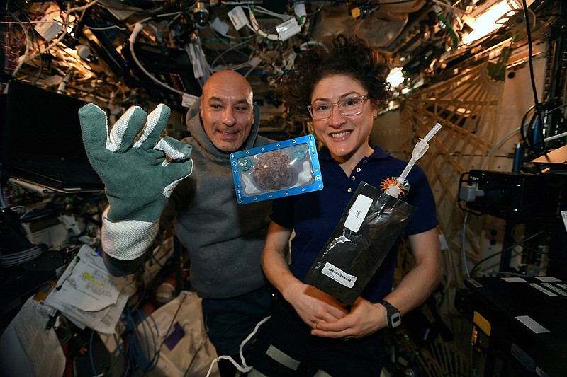 In this photo made available by U.S. astronaut Christina Koch via Twitter on Dec. 26, 2019, she and Italian astronaut Luca Parmitano pose for a photo with a cookie baked on the International Space Station. Researchers want to inspect the handful of chocolate chip cookies baked by astronauts in a special Zero G oven. (NASA via AP)