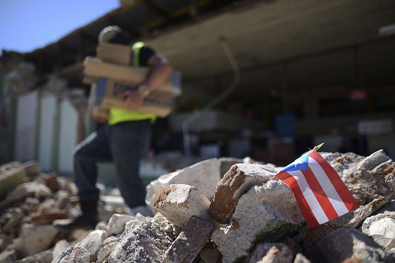 A Puerto Rican flag hangs within the rubble, after it was placed there where store owners and family help remove supplies from Ely Mer Mar hardware store, which partially collapsed after an earthquake struck Guanica, Puerto Rico, Tuesday, Jan. 7, 2020. A 6.4-magnitude earthquake struck Puerto Rico before dawn on Tuesday, killing one man, injuring others and collapsing buildings in the southern part of the island. (AP Photo/Carlos Giusti)