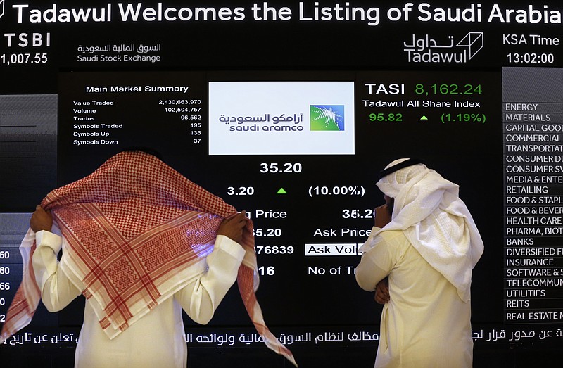 FILE- In this Dec. 11, 2019, file photo, the Saudi stock market officials watch the stock market screen displaying Saudi Arabia's state-owned oil company Aramco after the debut of Aramco's initial public offering (IPO) on the Riyadh's stock market in Riyadh, Saudi Arabia. Saudi Arabian oil company Aramco's initial public offering raised $29.4 billion, more than previously announced after the company said Sunday it used a so-called "greenshoe option" to sell an additional 450 million shares to satiate investor demand. (AP Photo/Amr Nabil)