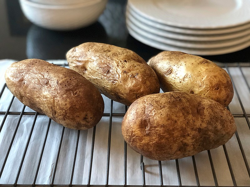 This Dec. 31, 2019 photo shows four baked potatoes resting on a rack in Amagansett, N.Y. Preheat the oven to 350 degrees Fahrenheit and place a sheet of heavy-duty aluminum foil on the bottom shelf of the oven in case any of the juices drip. After washing and drying the potatoes, coat them with either a little regular Crisco shortening or olive oil. Then prick them four or five times with a fork to let steam escape while they are baking. After an hour of baking, stick the end of a paring knife into the potato to gauge its doneness. It generally takes another 20 minutes to be perfect, but it depends on the potato's size. (Elizabeth Karmel via AP)