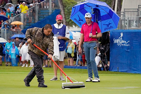 A course worker clears standing water off the 18th green before Bo Hoag putts during last Sunday's final round of the Sony Open in Honolulu.