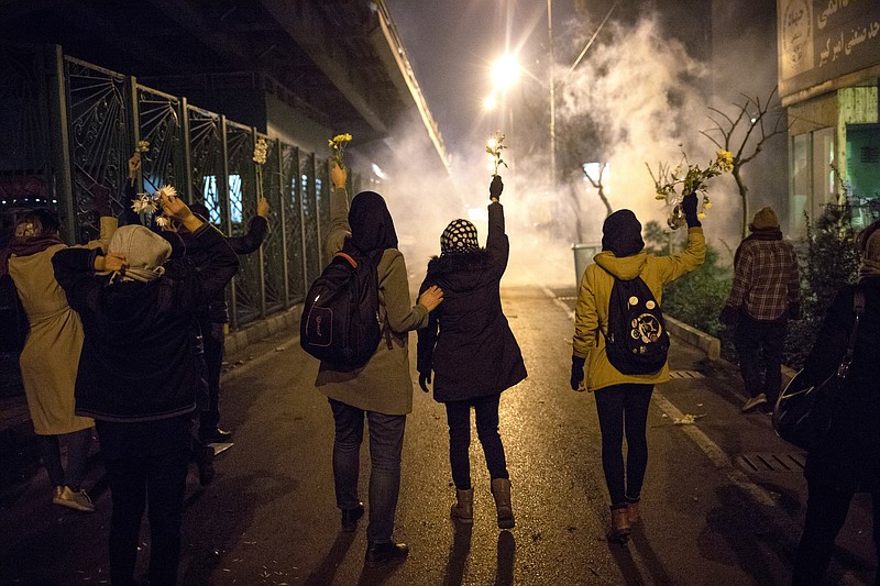 In this photograph taken Saturday, Jan. 11, 2020, protesters hold flowers as tear gas fired by police rises at a demonstration in front of Amir Kabir University in Tehran, Iran, to remember victims of a Ukrainian airplane shot down by an Iranian missile. On Monday, Jan. 13, 2020, online videos purported to show that Iranian security forces fired both live ammunition and tear gas to disperse demonstrators protesting against the Islamic Republic's initial denial that it shot down a Ukrainian jetliner. (AP Photo)