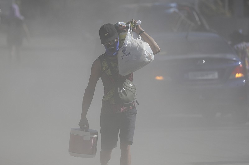 A man walks the his belongings through clouds of ash kicked up on a road as authorities enforced total evacuation of residents living near Taal volcano in Agoncillo town, Batangas province, southern Philippines on Thursday Jan. 16, 2020. Taal volcano belched smaller plumes of ash Thursday but shuddered continuously with earthquakes and cracked roads in nearby towns, which were blockaded by police due to fears of a bigger eruption. (AP Photo/Aaron Favila)