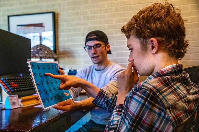 Mitchell Robins points to letters to form words that therapist Anthony Bartell, 23, can write down to draft a blog post in Robins's Highland Park home on Friday, Dec. 27, 2019. Robins has autism and uses his blog to educate and communicate with others who are non-verbal. (Camille Fine/Chicago Tribune/TNS)