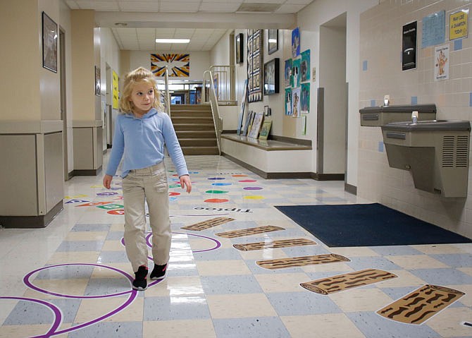 Elise Kempker, 5, looks toward St. Xavier School Principal Jordan Tobar on Thursday while demonstrating a tip-toe across the purple curled line sticker on the school's new sensory pathway in Taos. Kempker said one of her favorite activities included in the hallway is the crab walk.