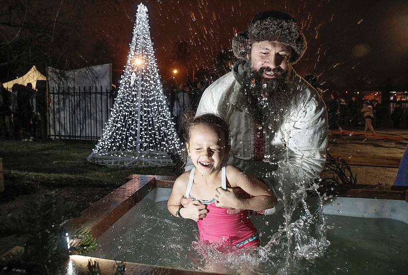 A man dips a girl in the ice water during a traditional Epiphany celebration in St. Petersburg, Russia, early Sunday, Jan. 19, 2020. Thousands of Russian Orthodox Church followers plunged into icy rivers and ponds across the country to mark Epiphany, cleansing themselves with water deemed holy for the day. (AP Photo/Dmitri Lovetsky)