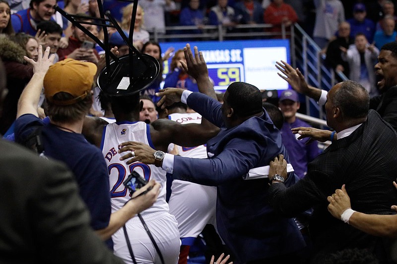 Silvio De Sousa of Kansas holds a chair in the air during a fight at the end of Tuesday's game against Kansas State in Lawrence, Kan. Two players from each team were given multiple game suspensions Wednesday.