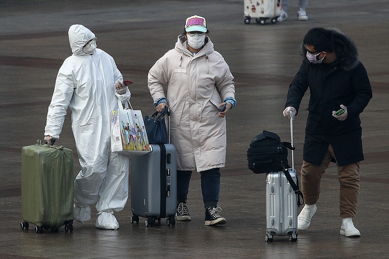 A passenger wearing a full-body protective suit catches the eyes of others as they walk out from the Beijing railway station in Beijing, Tuesday, Feb. 11, 2020. China's daily death toll from a new virus topped 100 for the first time and pushed the total past 1,000 dead, authorities said Tuesday after leader Xi Jinping visited a health center to rally public morale amid little sign the contagion is abating. (AP Photo/Andy Wong)
